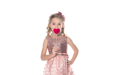 adorable little kid in pink dress holding red heart on stick and looking at camera isolated on white