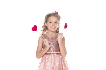 beautiful little kid in pink dress holding red hearts on sticks and smiling at camera isolated on white