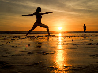 Fototapeta na wymiar Frau macht Yoga am Strand bei Sonnenuntergang