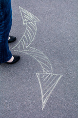 Woman in shoes standing on the asphalt road. On the road with chalk drawn signs arrows.
