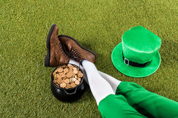 cropped view of leprechaun with pot of gold and hat sitting on green grass