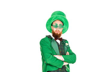 bearded man in green costume and clover shaped eyeglasses standing with crossed arms isolated on white, st patricks day concept