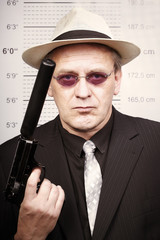 Rent killer man portraited with silenced pistol in front of mug board