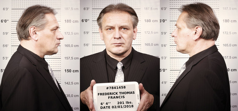 Older criminal man portraited in police station style in front of mug board and data tablet