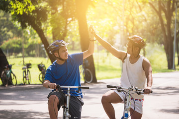 Friends are touching hands together while cycling together in a shady park.