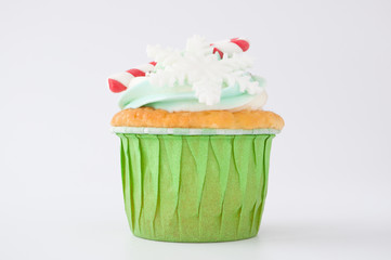 New year or christmas green cupcakes with whipped cream, decorated with candy cane, a snowflake, silver confectionery balls on white background. 