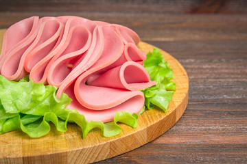 Sliced sausages with salad leaves on the wood background.