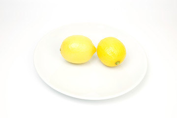 Two lemons on a white plate on a white backdrop.