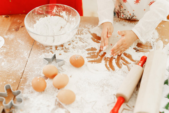 Cropped shot of little child in apron bakes something delicious on kitchen, makes cakes with hands, surrounded with rolling pin, eggs and flour, uses special cutter to make cookie of different shape.