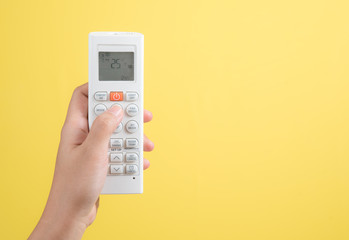 Hand with air conditioner remote control on yellow background,adjust air conditioner to 25 degrees...