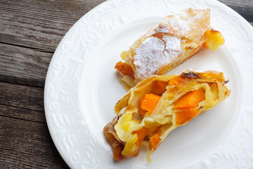 Strudel pumpkin and apple with raisins on parchment, fruit and vegetables on a dark wooden board