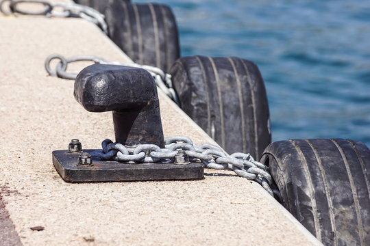 Old metal dock mooring pole with ring and rope for securing fishing boats