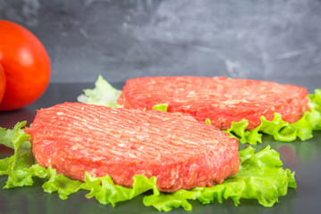 Raw burgers on parchment paper with tomatoes, chili peppers and rosemary. Grey marble background