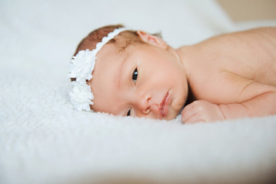 Sweet newborn baby girl with a bow on her head lies on a light blanket with her eyes open