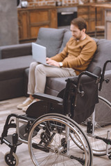 Obraz premium close-up view of wheelchair and disabled man using laptop on sofa at home