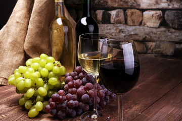 Red Wine bottle and white wine with grapes and glasses on wooden background