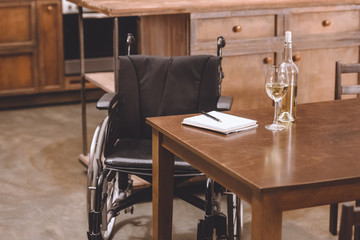 wheelchair standing near table with wine bottle, glasses, notebook and pen
