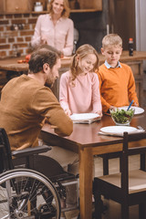 happy kids with father in wheelchair serving table for dinner at home