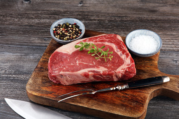 Raw fresh meat Ribeye Steak, seasoning and meat fork on dark background