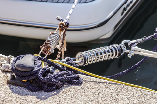 Metal cleat for mooring boats, bolted to the ground, with rope and shock absorber spring