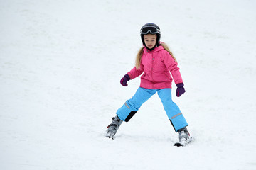 Fototapeta na wymiar Child skiing in the mountains. Girl in colorful suit and safety helmet learning to ski. Winter sport for family with young children. Kids ski lesson in ski school.