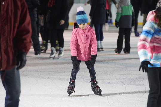 Child young girl ice skating at the ice rink outdoors. Child learning to skate on public rink.  Ice skaters using a temporary rink during the Christmas and New Year holiday period
