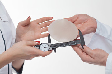 Plastic surgeon hands with silicon breast implants and calliper