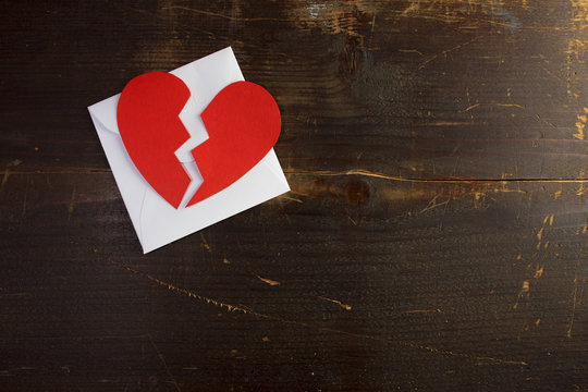 A break up valentine envelope letter with a broken torn paper heart ontop of it on a wood background texture template for graphic design