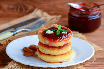Sweet cottage cheese pancakes with berry jam, almonds nuts and fresh mint on a serving plate. Simple breakfast pancakes recipe. Closeup