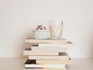 Buchstapel mit weißem Hintergrund und einem Glas Milch und eine Schale Kekse darauf. Schule, Bildung, Lernstress.