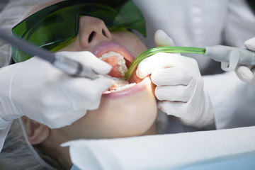 Naklejka premium Young female patient visiting dentist office.Beautiful woman with healthy straight white teeth sitting at dental chair with open mouth during a dental procedure.Dental clinic. Dental caries