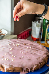 Frau mit rotlackierten Fingernägeln streut gehackte Mandeln auf Kuchenglasur in Küche