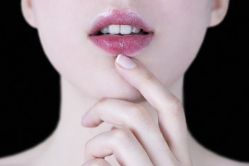 Close up of a young woman's pink lips with white teeth and hand gently touching her chin on black background