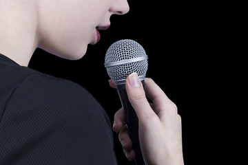 Close up of a young woman holding microphone and singing with black background