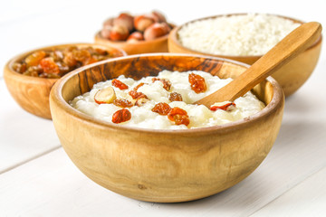 Rice milk porridge with nuts and raisins in wooden bowls on a white wooden table.