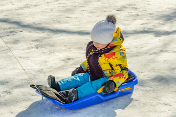A little boy skating on a sled with a knit scarf and hat on a winter day, outdoor games. Concept games outside.