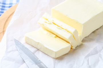 A bar of butter on a wooden board with a knife, on a white table. Ingredients for cooking.