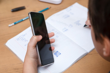 Schoolboy with smartphone doing homework at home.