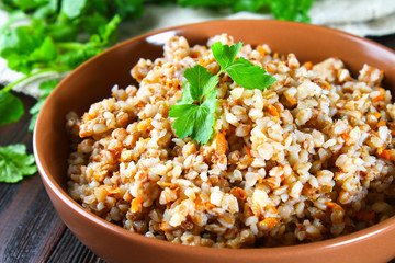 Boiled buckwheat in a bowl with pieces of chicken meat and cilantro on a brown wooden table.