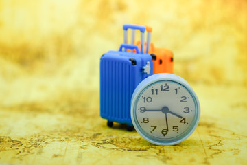 Time and travel concept. Close up of vintage round clock with miniature toy baggage on world map.