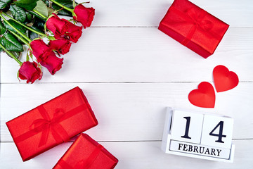 Red gift boxes with ribbon bow, two paper hearts, bouquet of res roses and wooden block calendar on white background. Greeting card mockup for Valentines Day. Love concept. Top view, flat lay