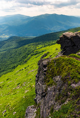 Obraz premium rocky cliff over the grassy valley. beautiful summer landscape with mountain ridge in the distance