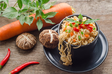 Instant noodles in black bowl on wooden background.