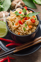 Instant noodles in black bowl on wooden background.