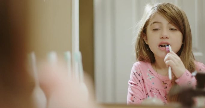 Young Girl Brushes Her Teeth in Mirror. view moves right and reveals a little girl brushing her teeth looking into a mirror