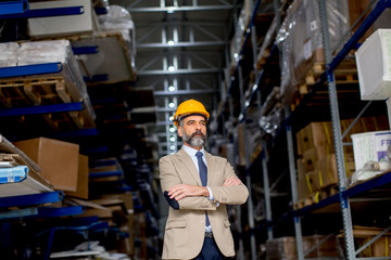 Portrait of senior businessman in suit with helmet in a warehouse