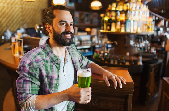 smiling man drinking green beer at bar or pub