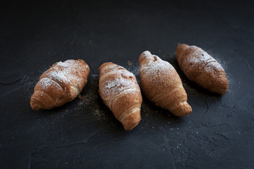 four croissants with a fruit filling, sprinkled with powdered sugar on a dark gray background