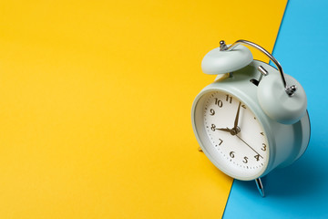 vintage alarm clock on two tone solid color yellow and light blue background