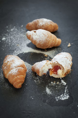 four croissants with a fruit filling, sprinkled with powdered sugar on a dark gray background